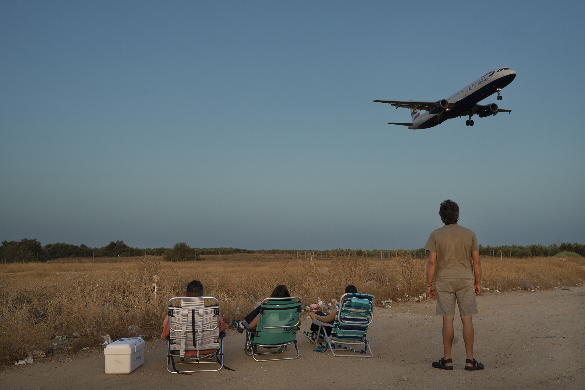Vecinos de Sevilla se reúnen en un descampado próximo al aeropuerto para contemplar la llegada de aviones en las tardes de verano en el municipio de San José de la Rinconada, comarca de la Vega del Guadalquivir. Agosto, 2025. Fotografia: LAURA LEÓN

 37°24'56.43"N
  5°52'14.95"O